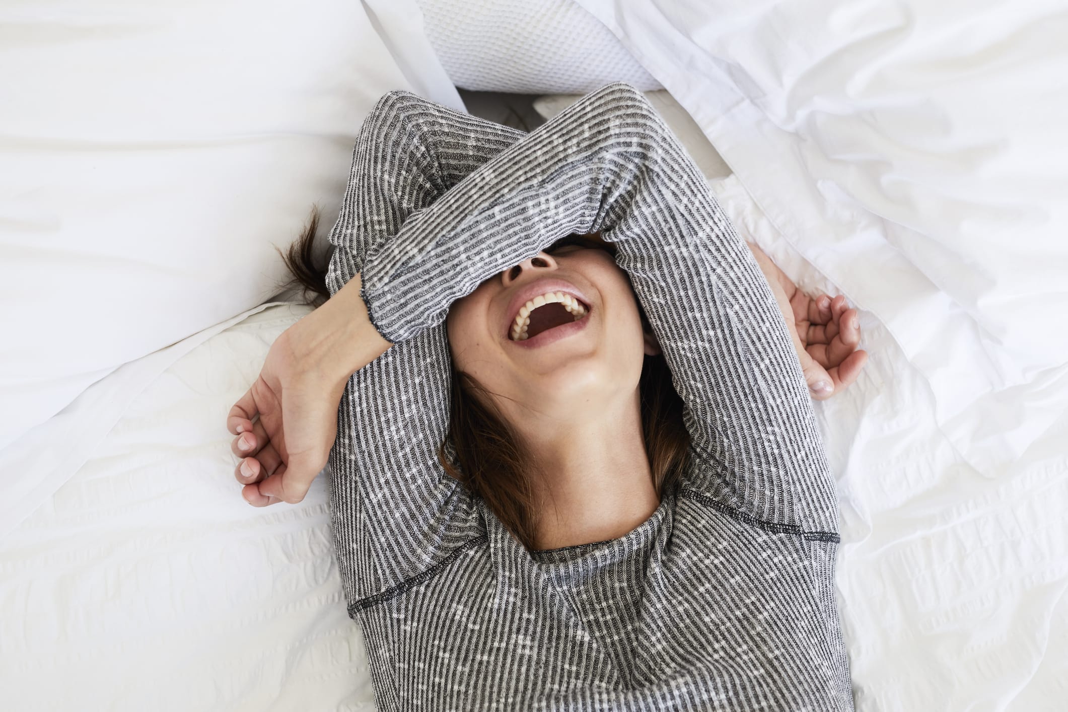 Woman wearing long-sleeved top laughing gleefully in bed