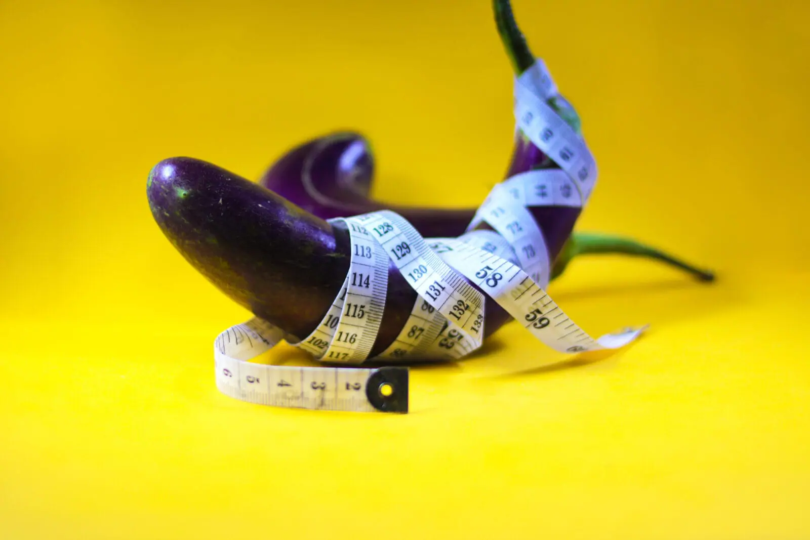 Eggplant wrapped with a measuring tape against yellow background
