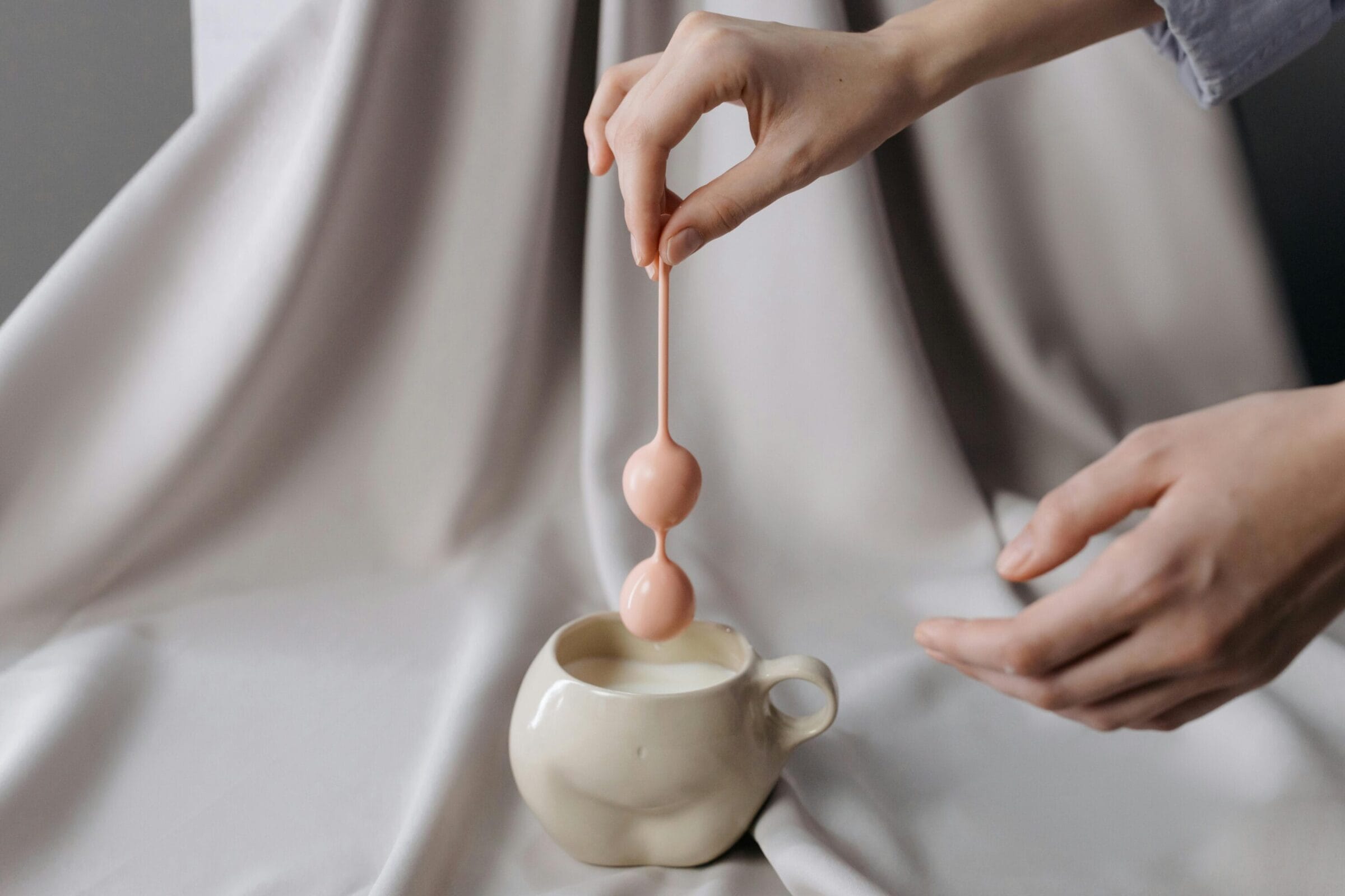 Person holding kegel balls over cup in the shape of female body