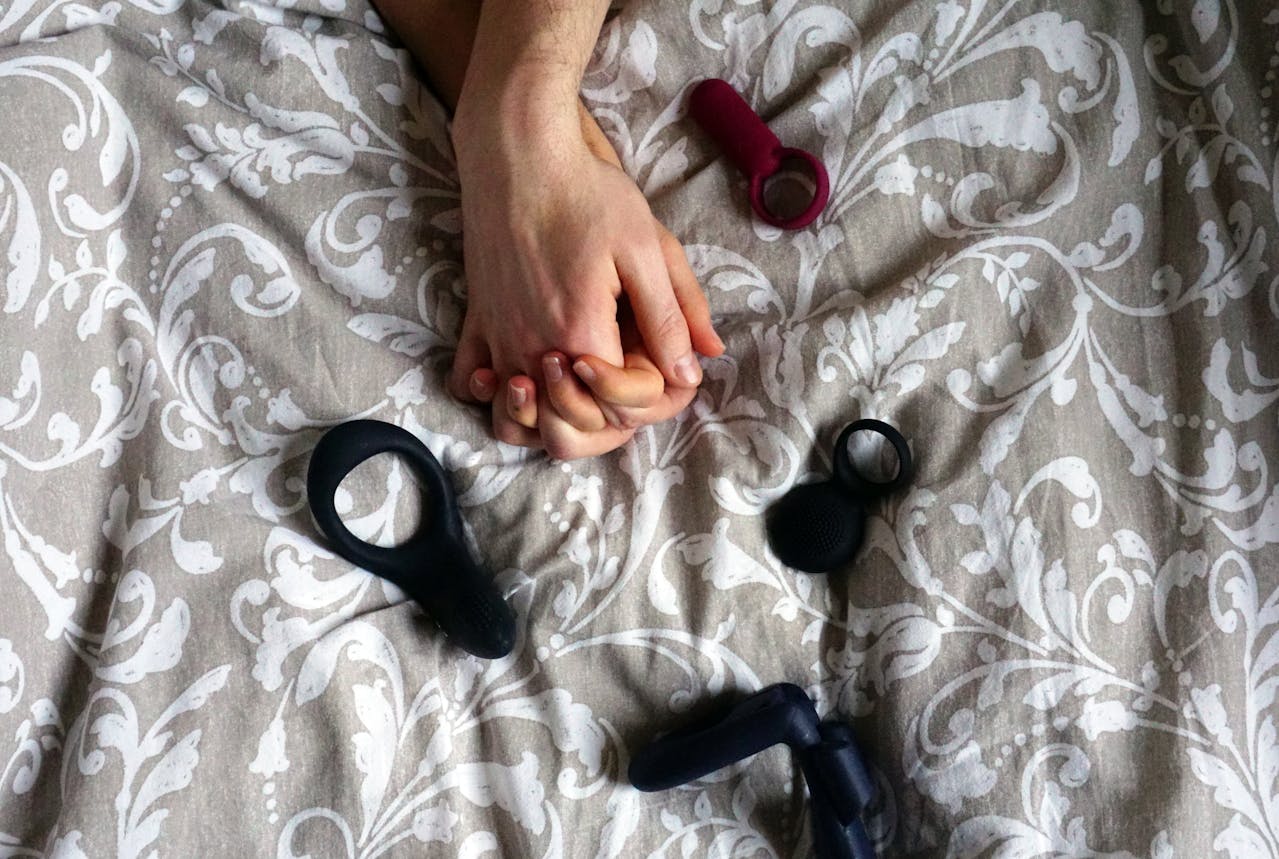 Close-up of couple’s hands against bedspread with sex toys